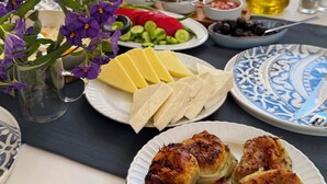 Uma mesa com diversos alimentos, uma garrafa de azeite e um prato de doces grelhados.