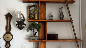 Uma prateleira de madeira com uma pintura, um relógio, um vaso, uma planta e uma bengala.