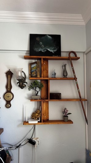 A wooden shelf with a painting, a clock, a vase, a plant, and a cane. - Şenol Pansiyon (Bozcaada)
