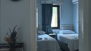 Quarto com piso de madeira, duas camas, uma mesa com um vaso e um relógio na parede.