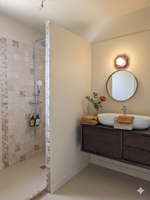 Une salle de bain équipée d’une douche, d’un lavabo, d’un miroir et d’articles de toilette.