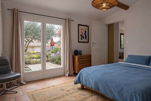Une chambre à coucher comprenant un lit, une chaise, une commode et une porte donnant sur un jardin.