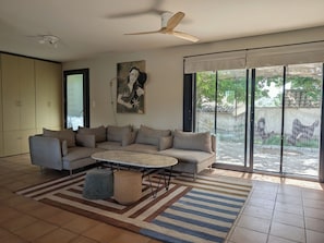 Ein Wohnzimmer mit Ecksofa, rundem Couchtisch, Deckenventilator und einer großen Glasschiebetür, die zu einem Außenbereich führt.