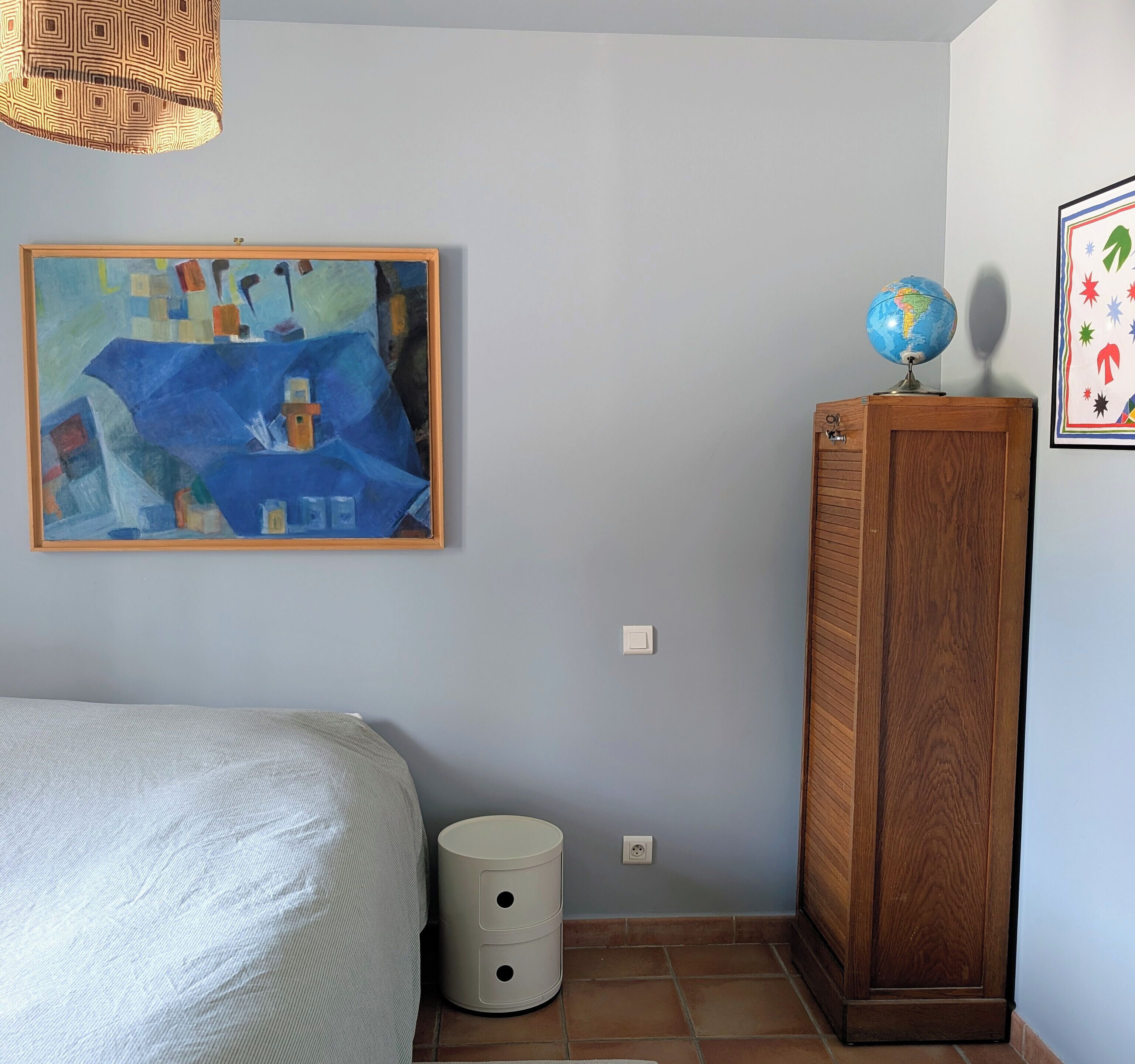 Ein Schlafzimmer mit einem Bett, einem Gemälde, einem Globus und einem Schrank.