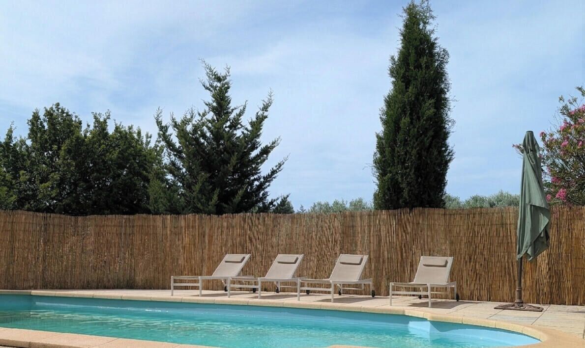 A swimming pool with lounge chairs and a bamboo fence.
