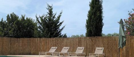 A swimming pool with lounge chairs and a bamboo fence.