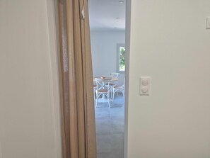 Ein Flur, der in einen Essbereich mit weißen Stühlen und einem Tisch führt, ein Fenster mit Blick auf Grünflächen und ein Lichtschalter an der Wand.