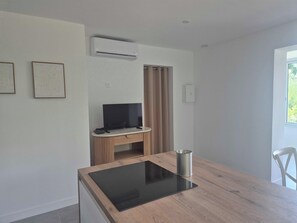 Ein modernes Zimmer mit einem Holztisch, einem Flachbildfernseher auf einem Holzbodenständchen, einer Klimaanlage und einem Fenster mit Vorhängen.