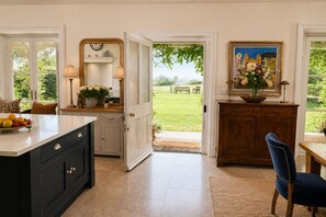 Une cuisine avec une porte ouverte donnant sur un jardin, un coin repas avec une table et des chaises, et un tableau accroché au mur.