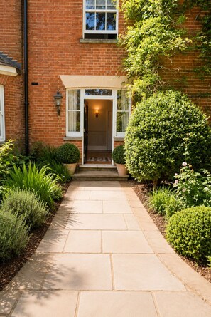 A brick house with a front porch, a door, and a pathway leading to the entrance. - Luxury home in the Country with Cedar Hot Tub, Tennis Court and Gym (Midgham)