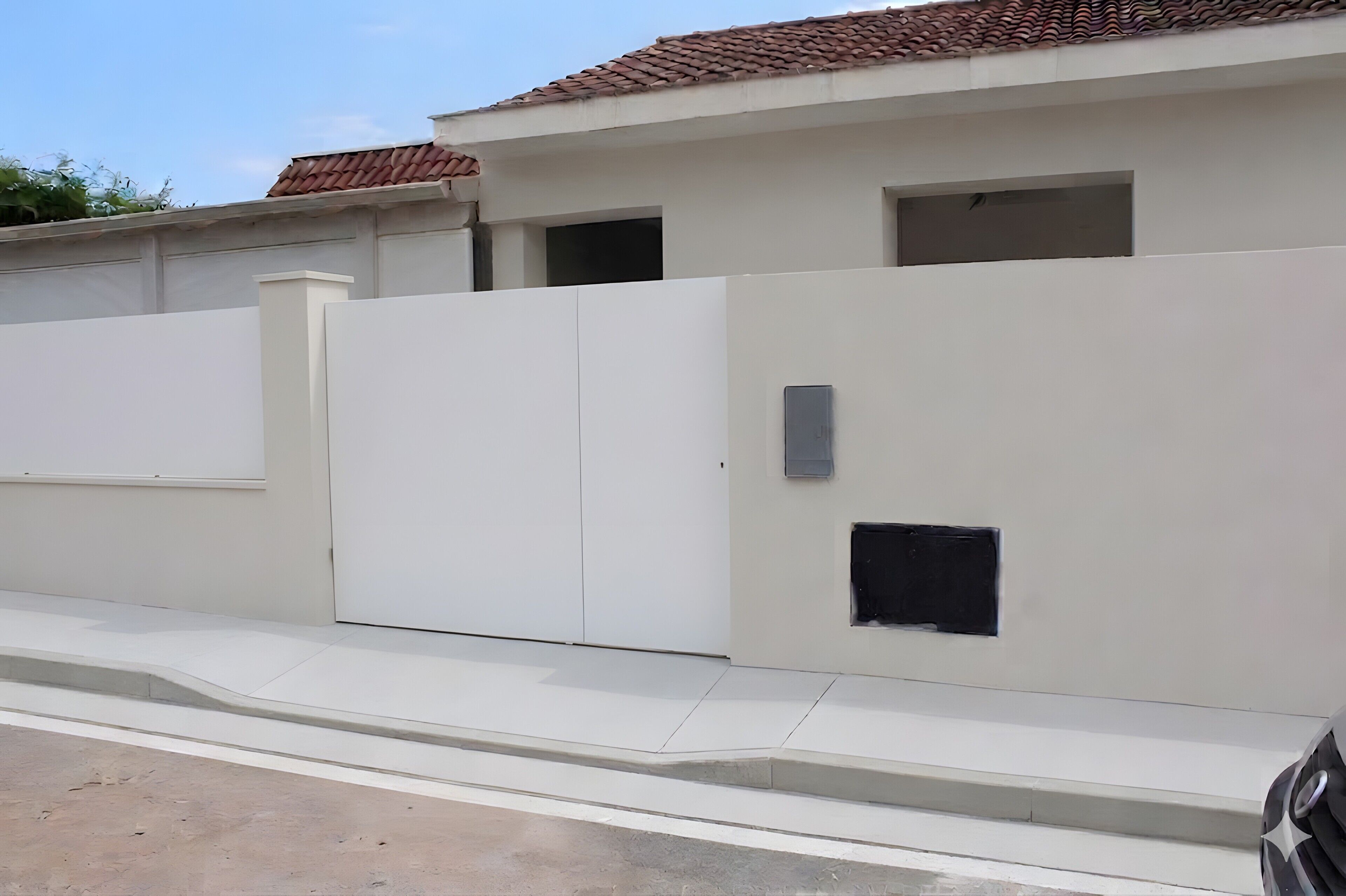 Un edificio bianco con tetto a tegole, ingresso con cancello e una piccola finestra.
