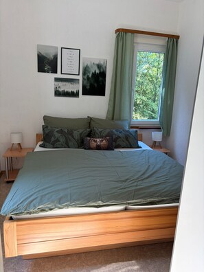 A bedroom with a bed, a nightstand, a lamp, a window with curtains, and three framed pictures on the wall.