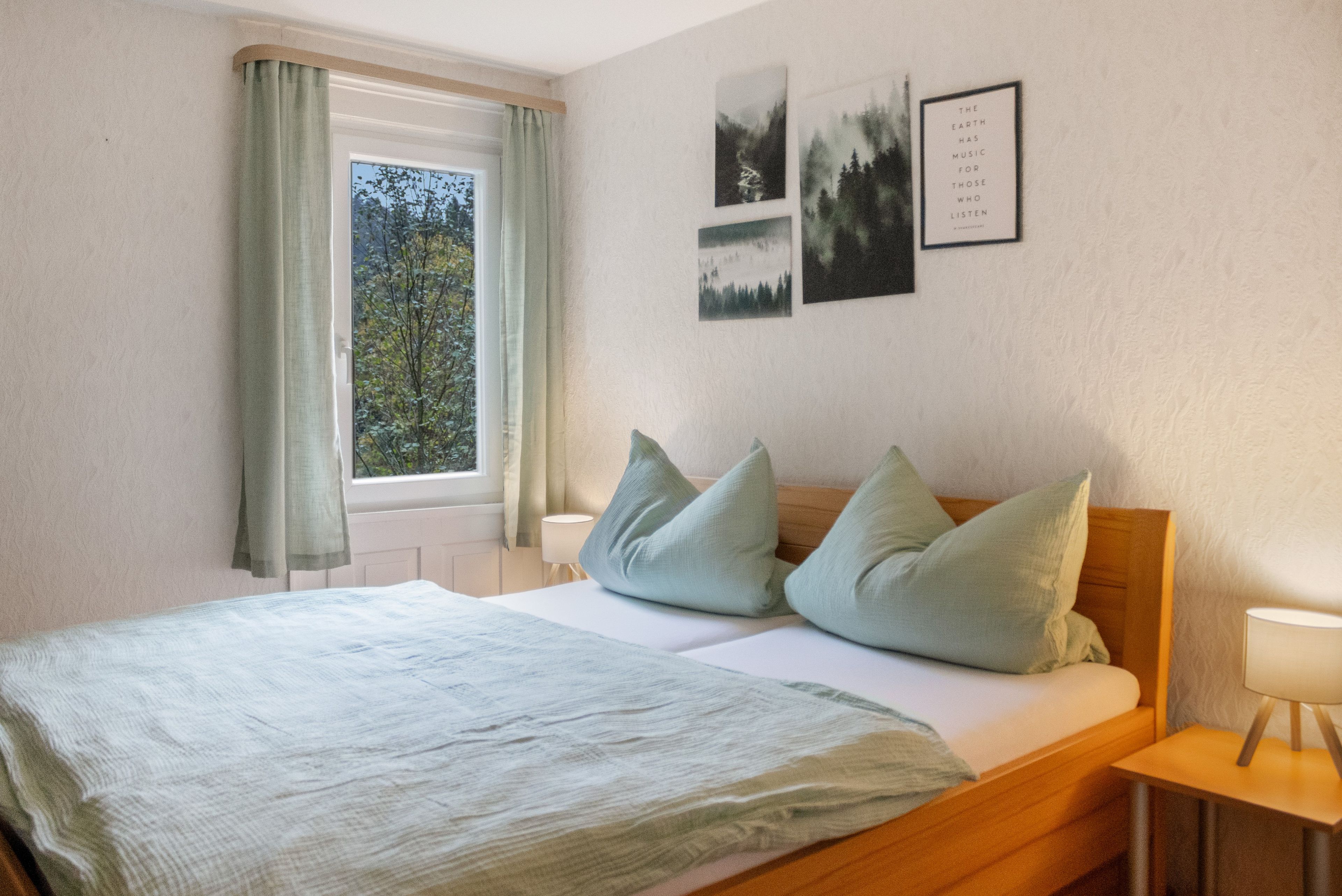 A bedroom with a bed, pillows, a window with curtains, and wall art.