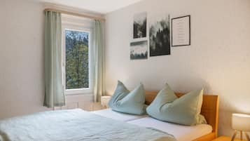 A bedroom with a bed, pillows, a window with curtains, and wall art.