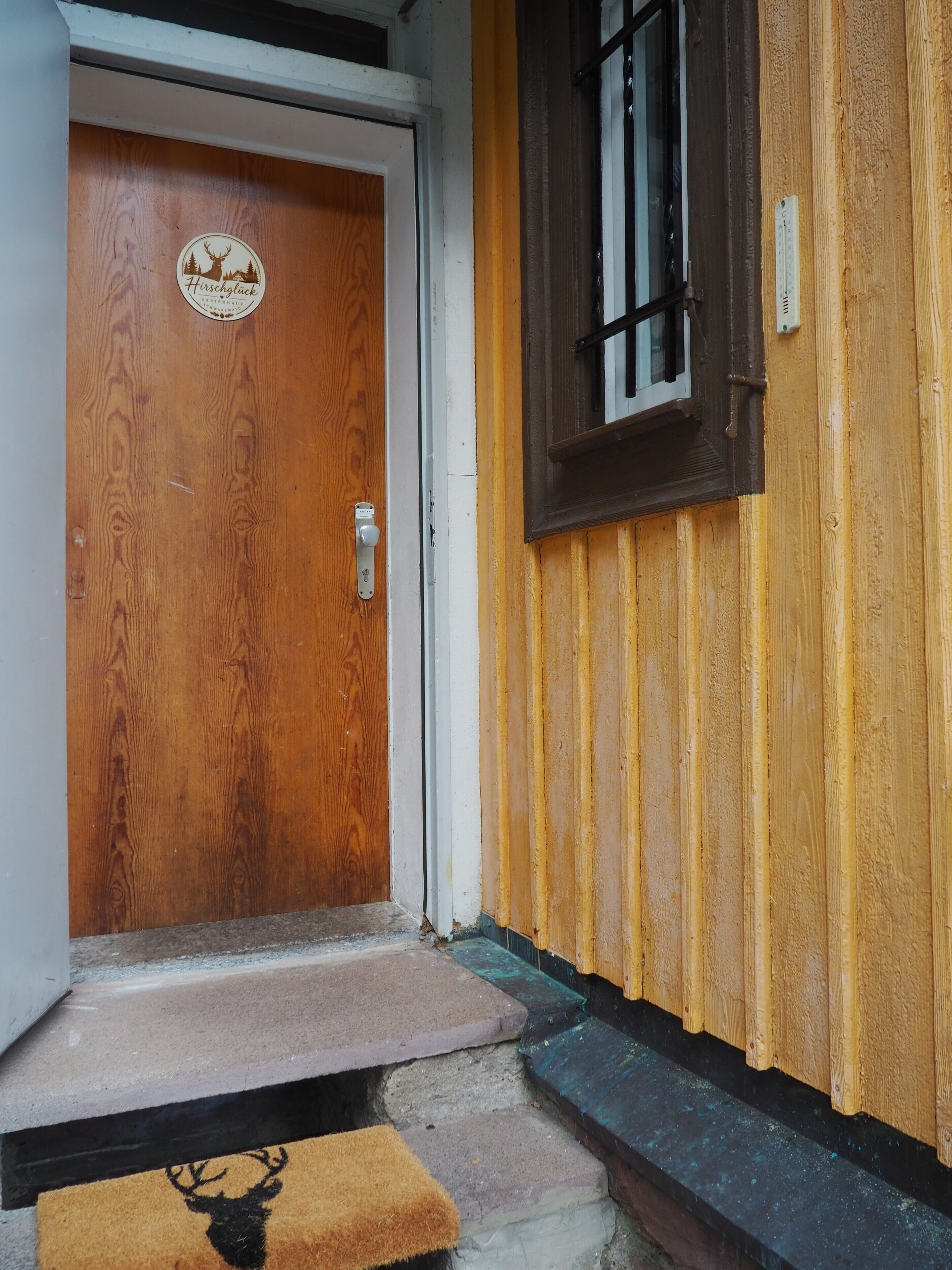 Une porte en bois ornée d’un logo, une fenêtre à cadre sombre et une petite marche menant à la porte.