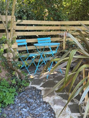 A wooden fence, a blue folding table, and chairs in a garden setting.