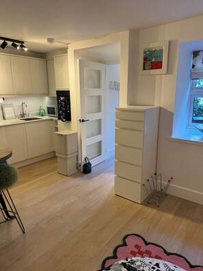 A modern kitchen with white cabinets, a microwave, and a sink. There is a door leading to another room and a window with a view.