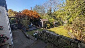 A garden with a stone wall, a wooden deck, and a small shed.