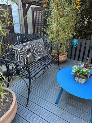 Een terras met een metalen bankje, een blauwe tafel en potplanten.