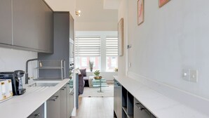 A modern kitchen with grey cabinets, a coffee machine, and a dining area with a glass table and chairs. - Stylish 1BR Penthouse with Balcony - City Centre near Cliffs Pavillion (Southend-on-Sea)