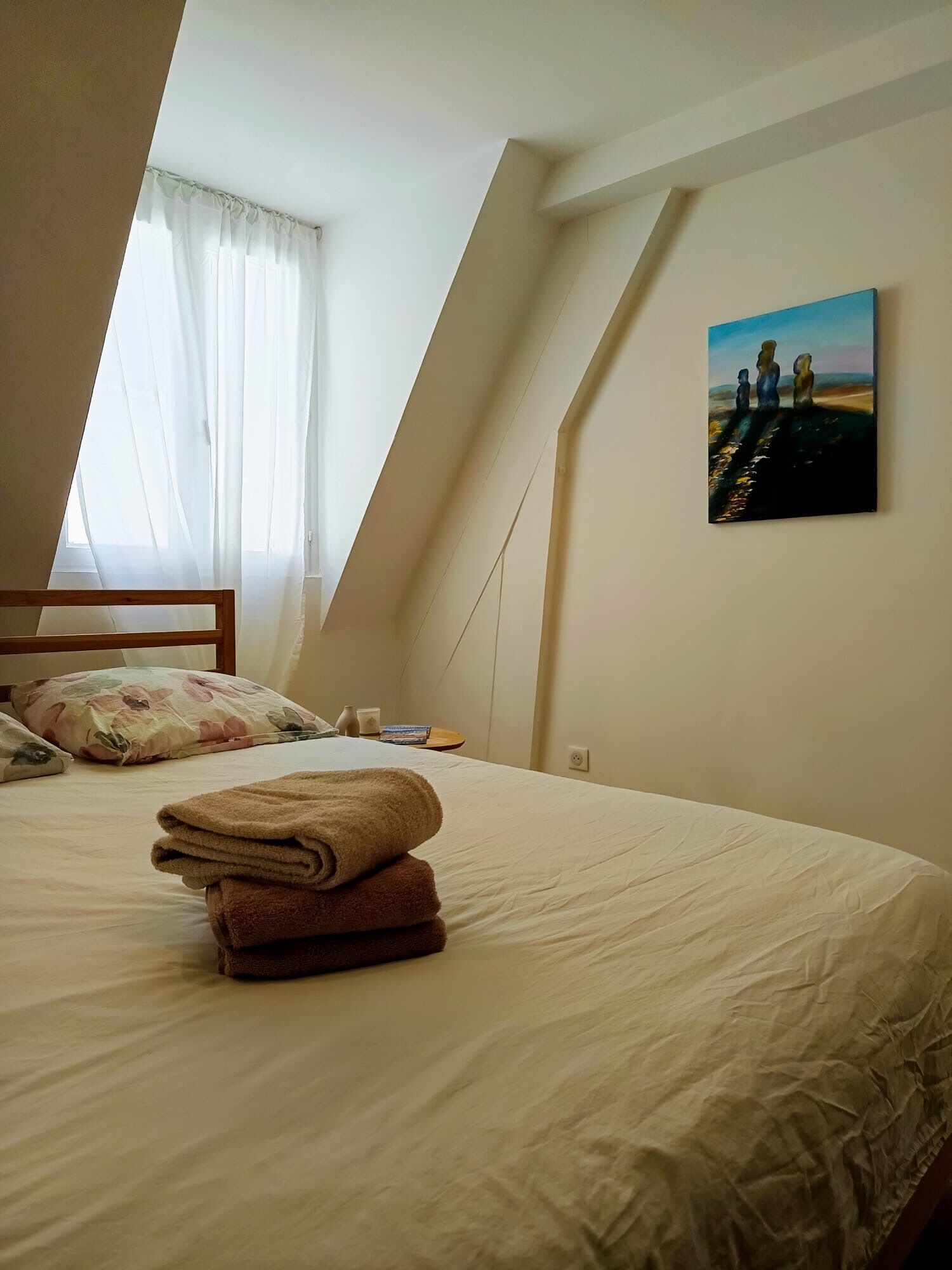A bedroom with a bed, pillows, a painting, and a window with curtains.