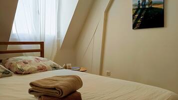 A bedroom with a bed, pillows, a painting, and a window with curtains.
