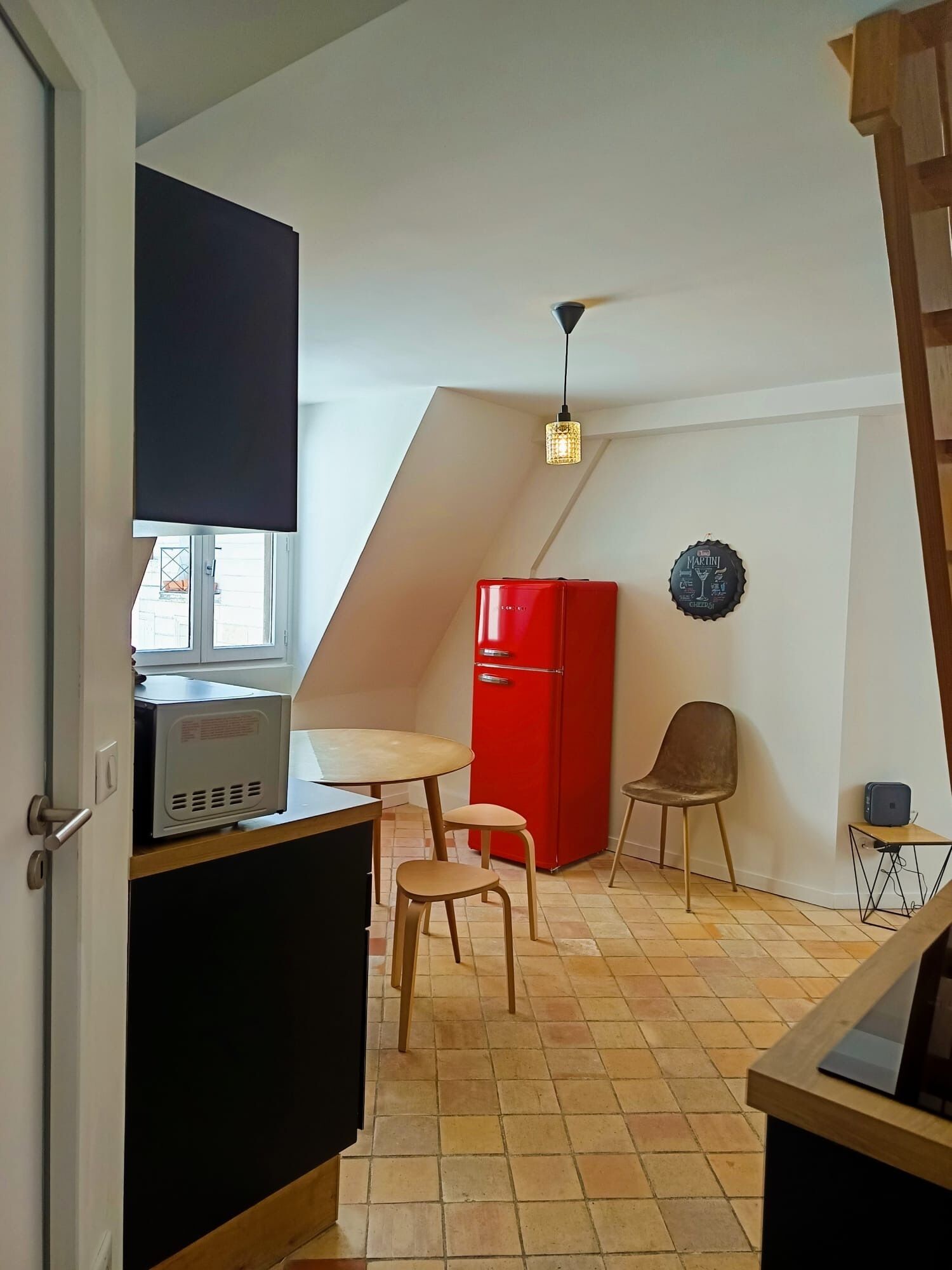 A compact kitchen with a microwave, a red refrigerator, a dining table with two chairs, and a ceiling fan.