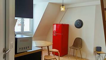 A compact kitchen with a microwave, a red refrigerator, a dining table with two chairs, and a ceiling fan.