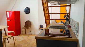 A compact kitchen with a red refrigerator, a wooden chair, a small table, and a tiled floor.