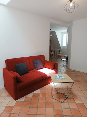 Ein rotes Sofa mit zwei Kissen, ein kleiner Holztisch und eine geometrische Pendelleuchte.