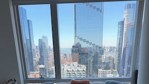 Una sala de estar moderna con un sofá blanco, una mesa de centro de vidrio con flores y vistas a la ciudad a través de amplias ventanas.