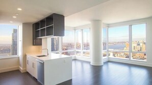 Una cocina moderna con una isla grande, armarios blancos y vistas a un paisaje urbano a través de amplios ventanales.