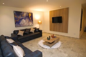 A living room with a sofa, a coffee table, a TV mounted on the wall, and a painting on the wall. - Settle inn Jebal Apartments (Cairo)
