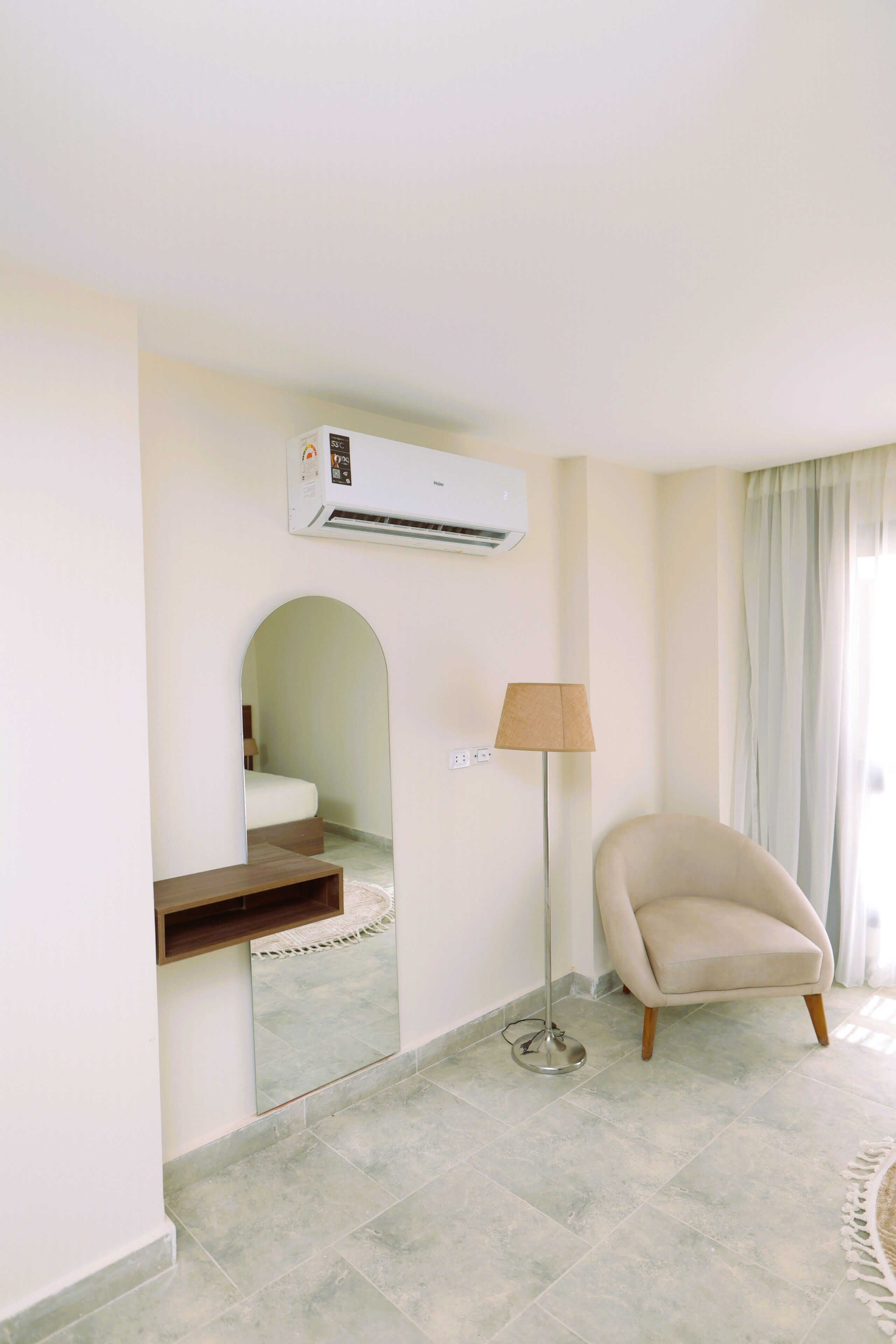 Una habitación de hotel con una cama, un aire acondicionado, una lámpara, una silla y un espejo.