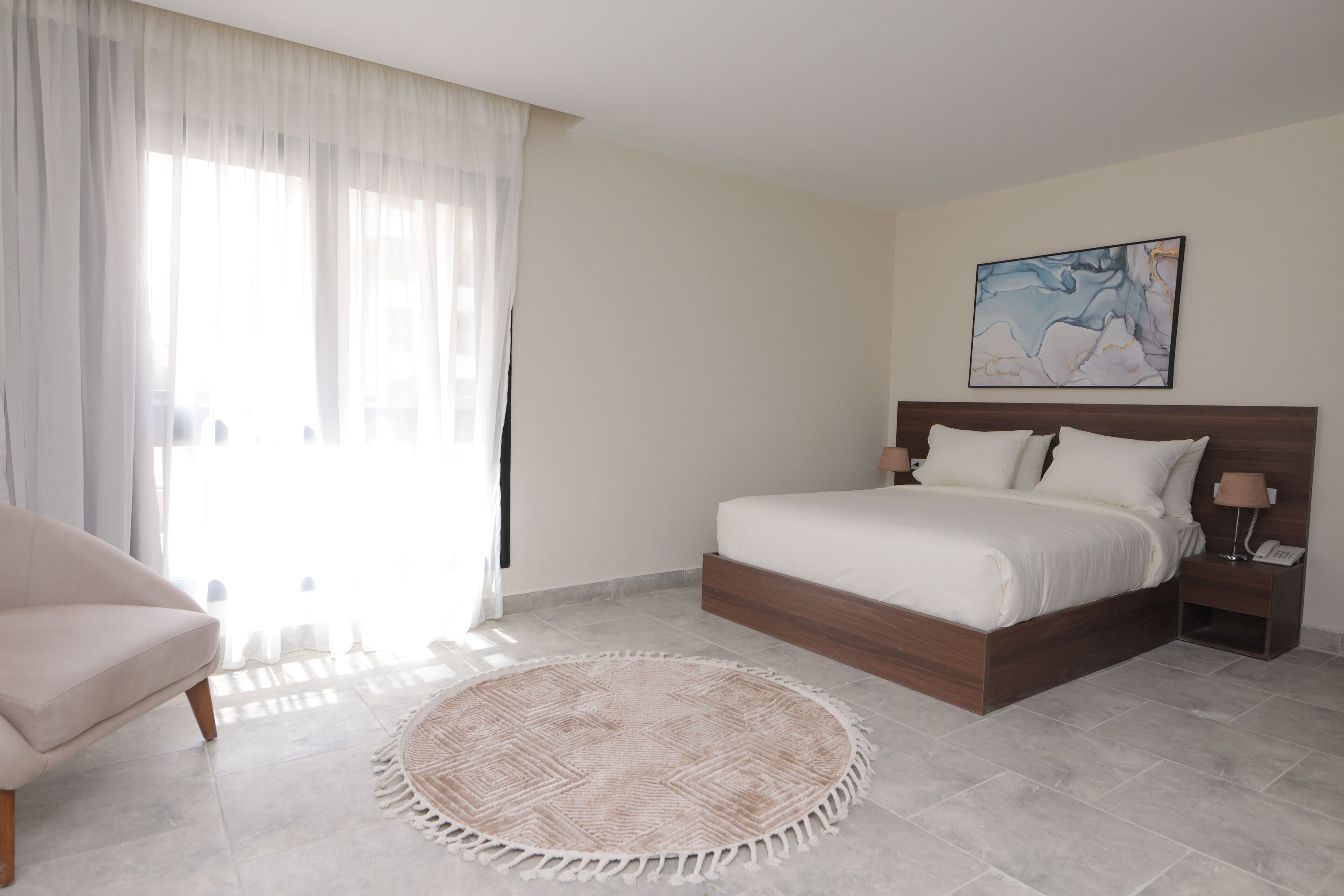 Un dormitorio con una cama, una mesita de noche, una silla y un tapete redondo.