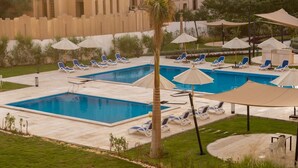 A pool area with multiple pools, lounge chairs, umbrellas, and a palm tree.