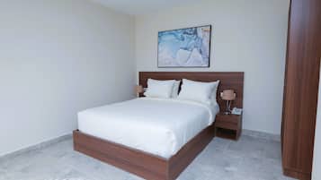Un dormitorio con estructura de cama de madera, ropa de cama blanca, una mesita de noche con lámpara y un cuadro en la pared.