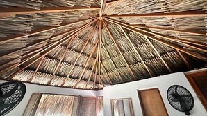 Et værelse med et stråtækt loft, træbjælker og en ventilator.