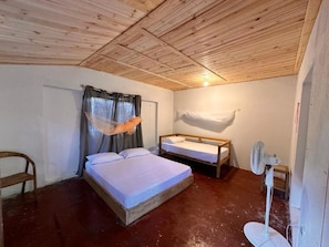 Et værelse med træloft, en seng, et sengebord, en stol, en ventilator og et vindue med gardiner.