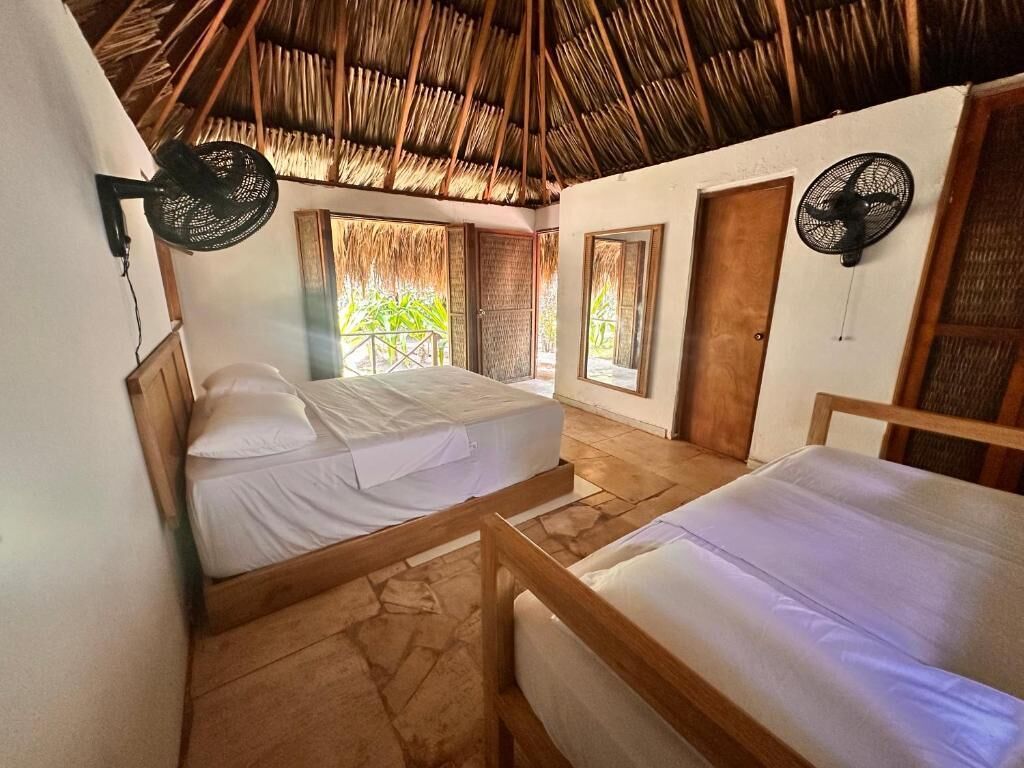 Une pièce avec deux lits en bois, un toit de chaume et deux ventilateurs fixés au mur.