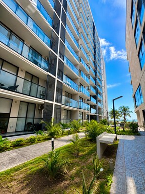 A modern multi-story building with balconies, a landscaped garden area, and a clear sky. - Apartamento moderno en pozos colorados (Santa Marta)