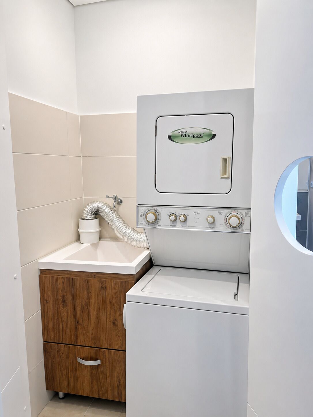 Un lavadero pequeño con lavadora y secadora Whirlpool, un armario de madera y un lavabo blanco.