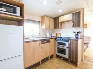 Een kleine keuken met een koelkast, fornuis, oven en een magnetron op een plank.
