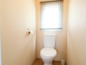 A small, clean bathroom with a toilet, a window with blinds, and a toilet paper holder. - Caravan 102 Seawick (Clacton-on-Sea)
