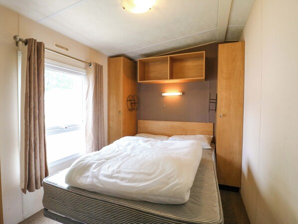 Quarto com cama, cortinas, cabeceira, prateleira na parede e luminária no teto.