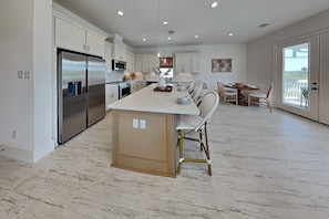 A modern kitchen with a central island, stainless steel appliances, and a dining area with a view. - Tiki Pool Club (Galveston)