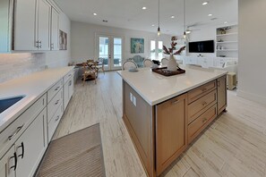 A modern kitchen with white cabinetry, a large island, and a dining area with chairs. - Tiki Pool Club (Galveston)