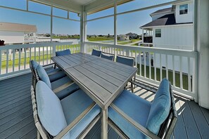 A covered outdoor deck with a table and chairs, a white railing, and a view of a residential area. - Tiki Pool Club (Galveston)