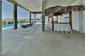 A covered outdoor area with a pool, lounge chairs, and a bar area with stools. - Tiki Pool Club (Galveston)