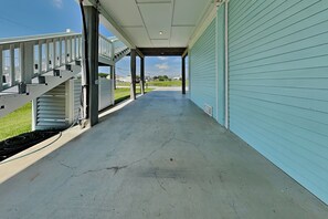 A covered porch with a concrete floor, a staircase, and a garage door. - Tiki Pool Club (Galveston)